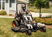 Male riding mower with property in the background