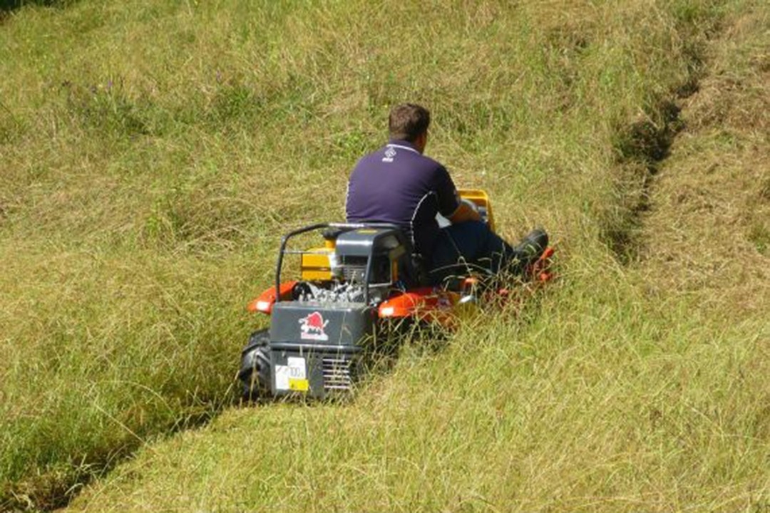 Male riding mower through long grass
