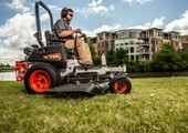 Male riding mower with building in background