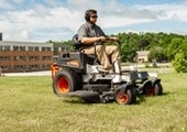 Male riding mower in front of building